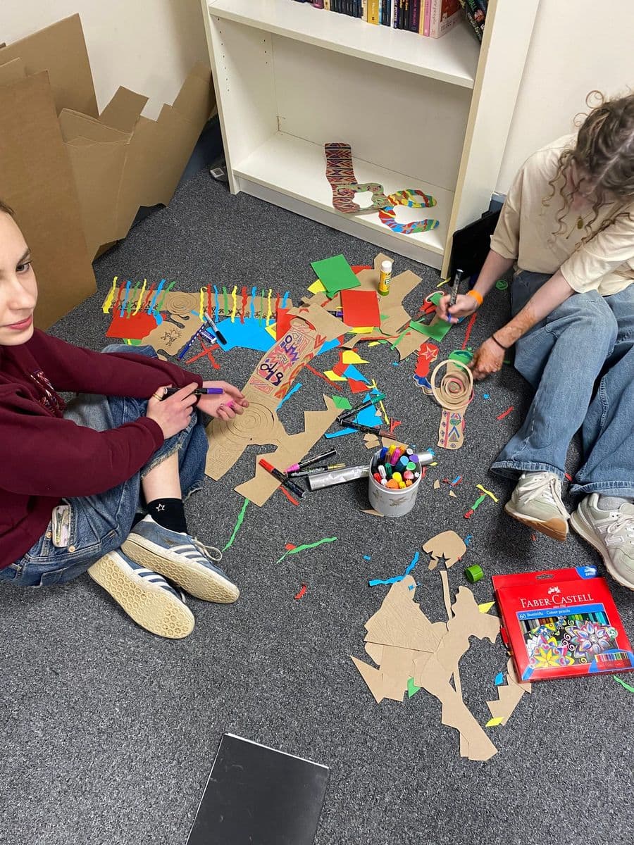 Young people sitting on the floor of the art room, building colourful card and paper constructions