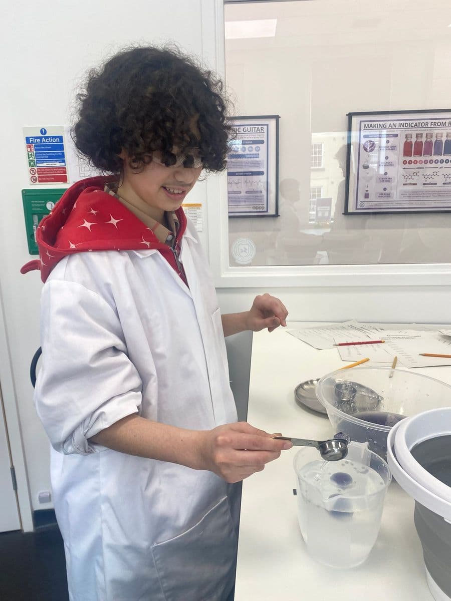 A young person in a white lab coat measuring out a sample with a scoop at the lab bench